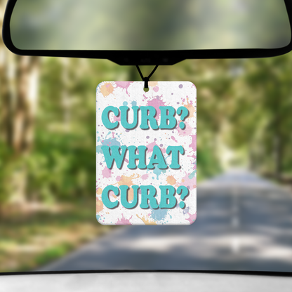 A mock up image showing a view through a car windscreen with a long tree lined road.  From the rearview mirror hangs an air freshener with the words CURB? WHAT CURB? in teal against a paint splattered background