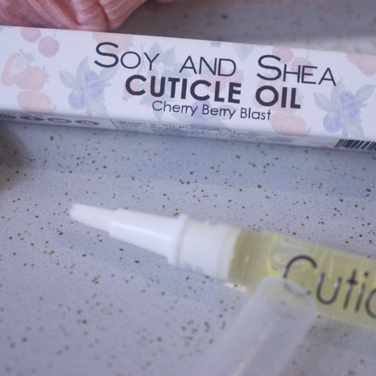 A close up image of the Cuticle oil pen showing the white brush tip. In the background is the box packaging with text CUTICLE OIL CHERRY BERRY BLAST and faded images of various berries