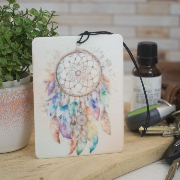 A car air freshener with a dream catcher design, featuring colorful feathers and a felt material, placed on a wooden surface.