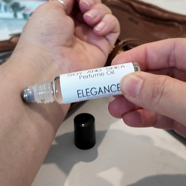 A person is applying a roller bottle of perfume oil labelled ELEGANCE to the other wrist. 