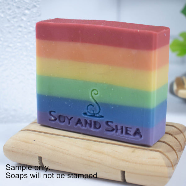 A soap bar with even layers of colours sit on a wooden soap dish with a blurred background