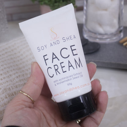 Hand holding a white tube of Soy and Shea Face Cream with a blurred background