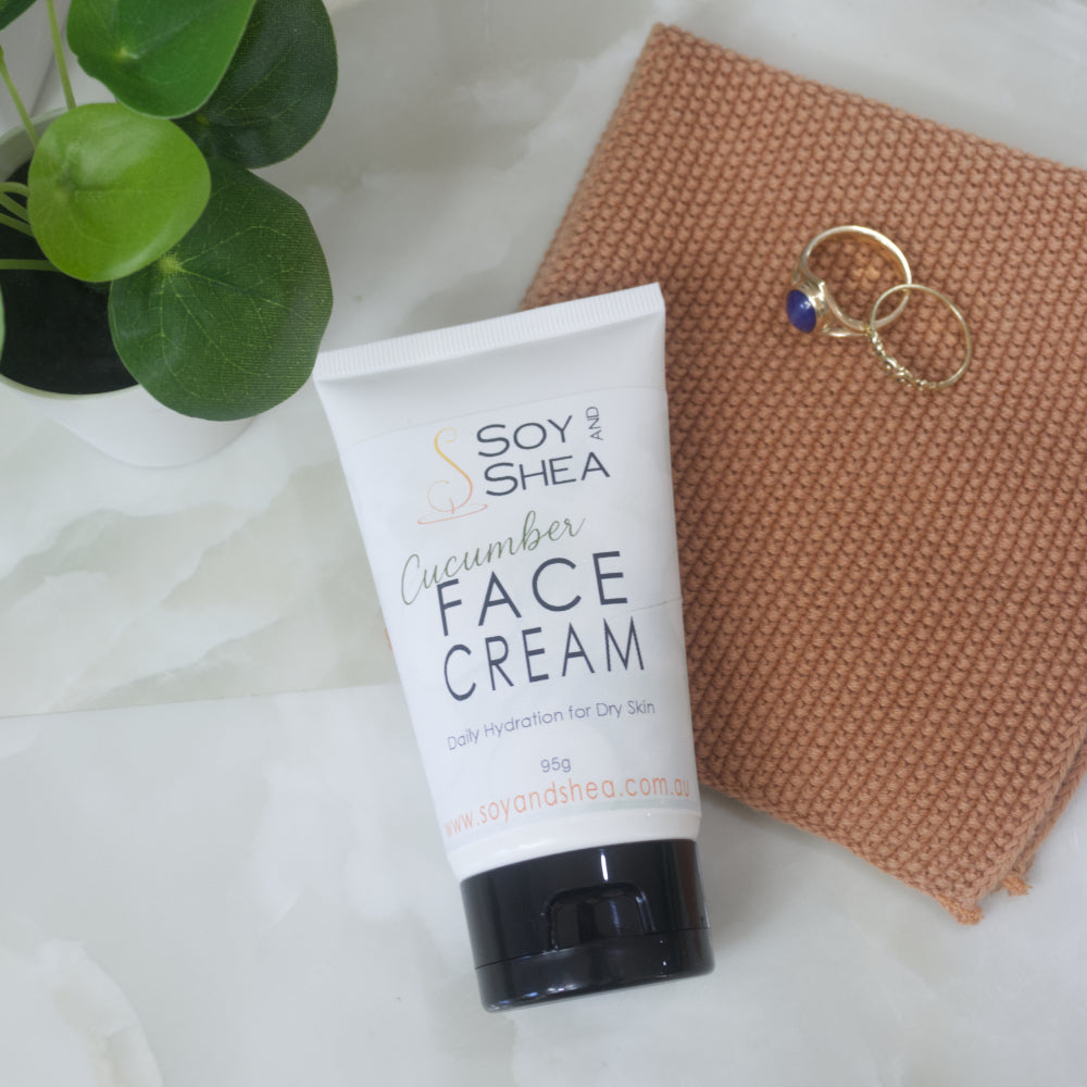 A 95g tube of Soy and Shea Cucumber Face Cream is displayed on a white marble surface next to a textured terracotta cloth and a green plant.