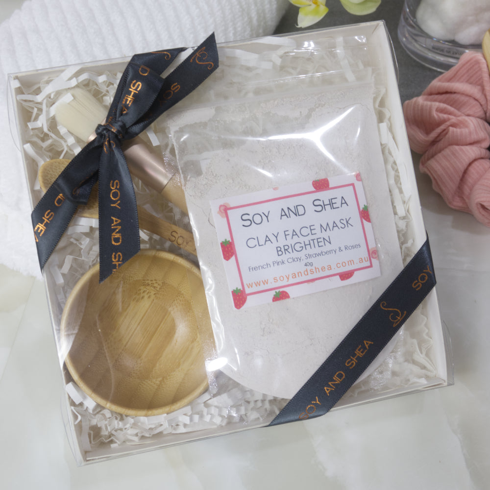 Soy and Shea clay face mask gift box with a clear bag of pale pink powder along with spoon and bowl all tied with dark grey ribbon