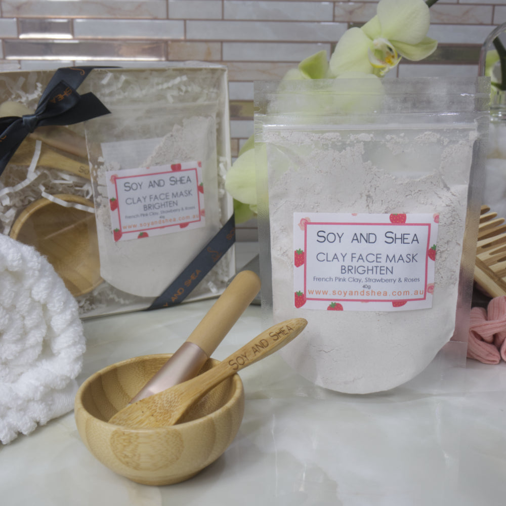 Soy and Shea clay face mask packaging on a bathroom counter with a wooden bowl and spoon.