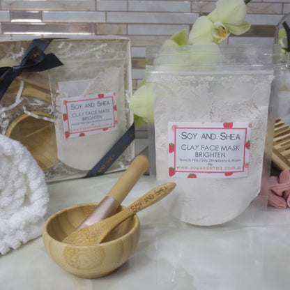 Soy and Shea clay face mask packaging on a bathroom counter with a wooden bowl and spoon.