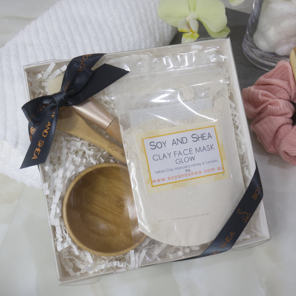 Soy and Shea clay face mask gift set  with satchet of yellow powder along with a wooden scoop and decorative ribbon on a white surface.