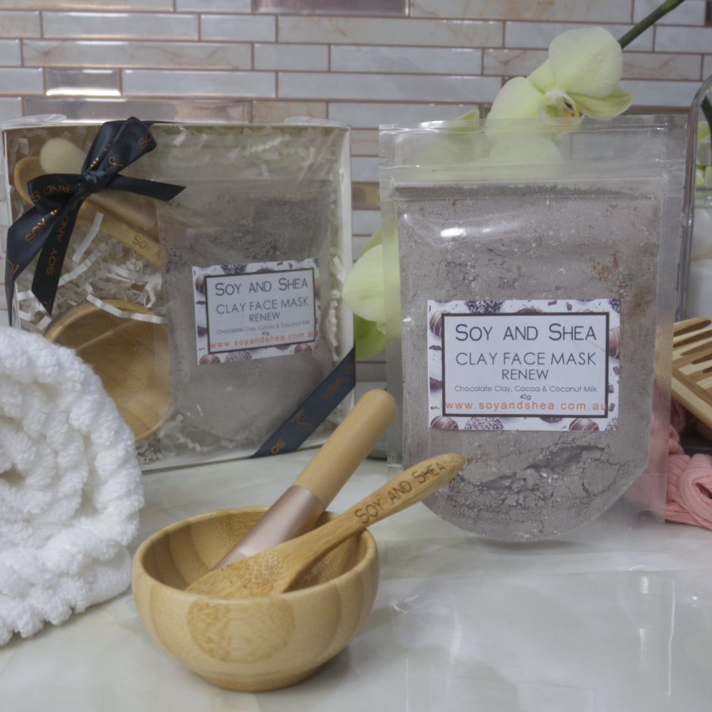 Soy and Shea Renew Clay Face Mask packaging with a wooden bowl and spoon on a bathroom counter.
