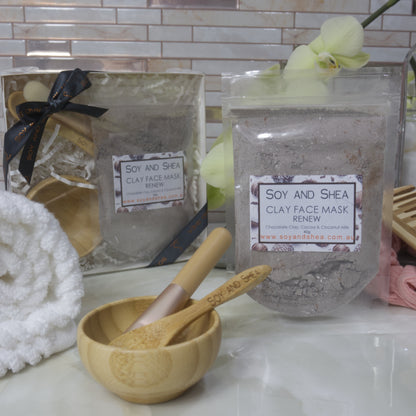 Soy and Shea Renew Clay Face Mask packaging with a wooden bowl and spoon on a bathroom counter.