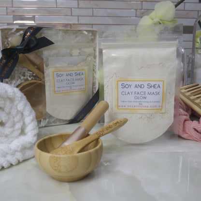Soy and Shea Glow clay face mask packaging with a wooden bowl and spoon on a marble surface.