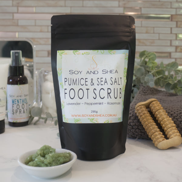 A black zip lock pouch labelled LAVENDER AND NETTLE FOOT SOAK sits on a bathroom counter along with a grey towel, wooden foot massager and bottle of Foot Spray.  In front of the pouch is a small white bowl filled with a green salt scrub.