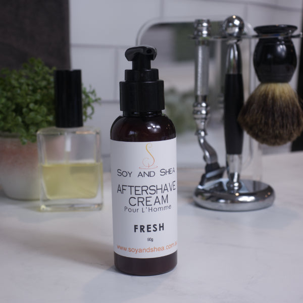 A bottle of aftershave cream labeled 'Fresh' from Soy and Sheen positioned on a bathroom counter with shaving accessories in the background.
