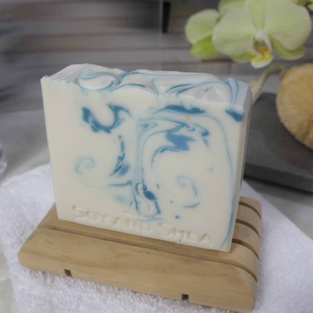 White bar of soap with blue swirls on a wooden stand, with a blurred background