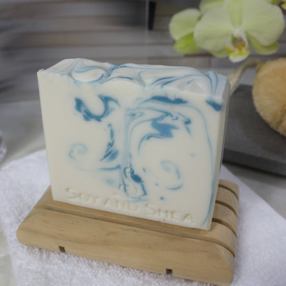White bar of soap with blue swirls on a wooden stand, with a blurred background