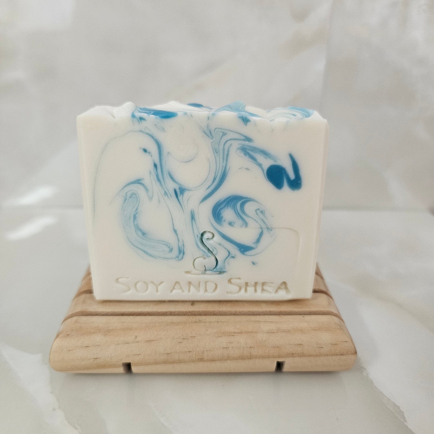 White Bar of soap with blue swirls on a wooden soap dish against a white background