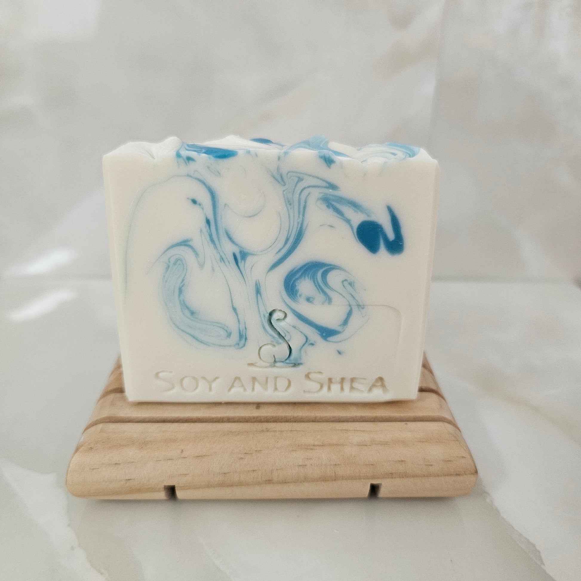 White Bar of soap with blue swirls on a wooden soap dish against a white background