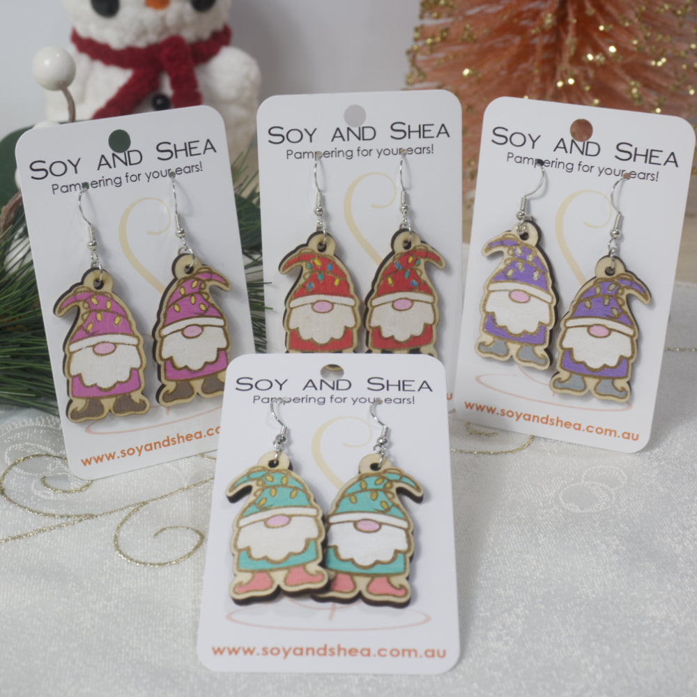 A selection of wooden Gnome-themed earrings on cards with 'Soy and Shea' branding. Each gnome is a different colour