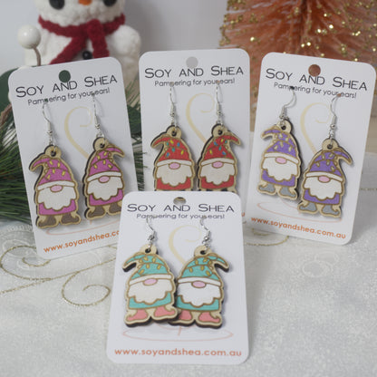 A selection of wooden Gnome-themed earrings on cards with 'Soy and Shea' branding. Each gnome is a different colour