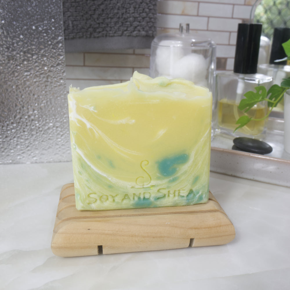 A soap stands on a wooden soap rack on a bathroom countertop.  The soap is a bright yellow with streaks of white and spots of green.