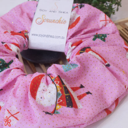 A close up image of the Grooving Santa Scrunchie showing images of a cartoon santa against a bright pink background with gold dots.