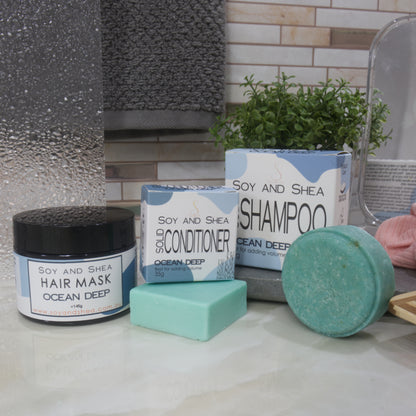 Soy and Shea hair care products including shampoo, conditioner, and hair mask on a bathroom counter. All products are in shades of blue-green.