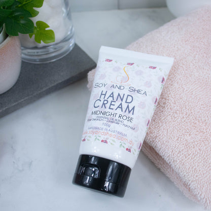 A white tubel with black lids lays across a white marble counter with the top resting on a pink towel.  The label features a soft design of scattered roses