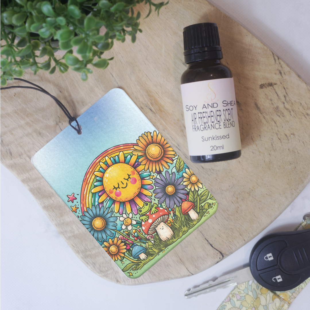 A car air freshener with a cartoon image of a smiling sun looking down on toadstool with frog lays on a wooden bench next to a bottle of scent.