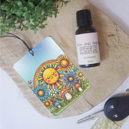 A car air freshener with a cartoon image of a smiling sun looking down on toadstool with frog lays on a wooden bench next to a bottle of scent.