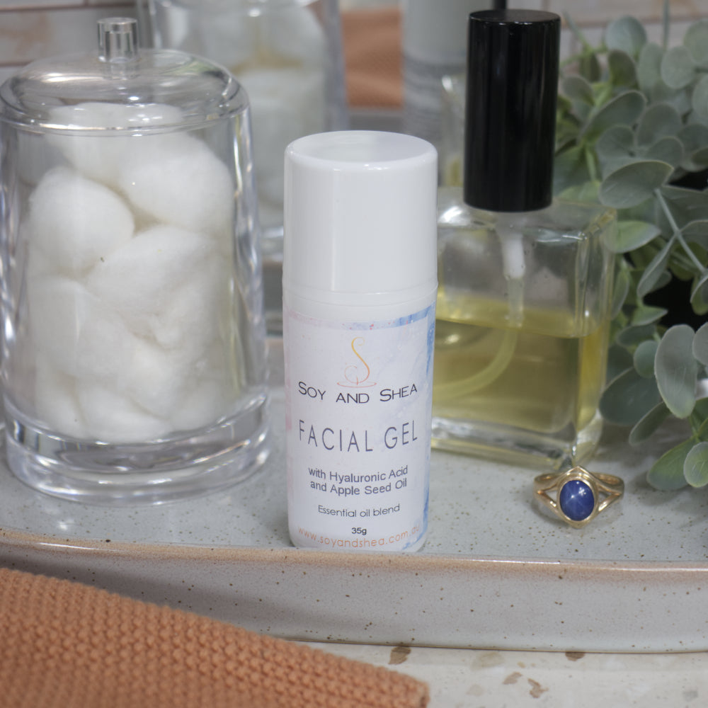 A white bottle of Facial gel bottle on stone tray surrounded by cotton balls, perfume and a plant in the background