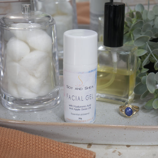 A white bottle of Facial gel bottle on stone tray surrounded by cotton balls, perfume and a plant in the background