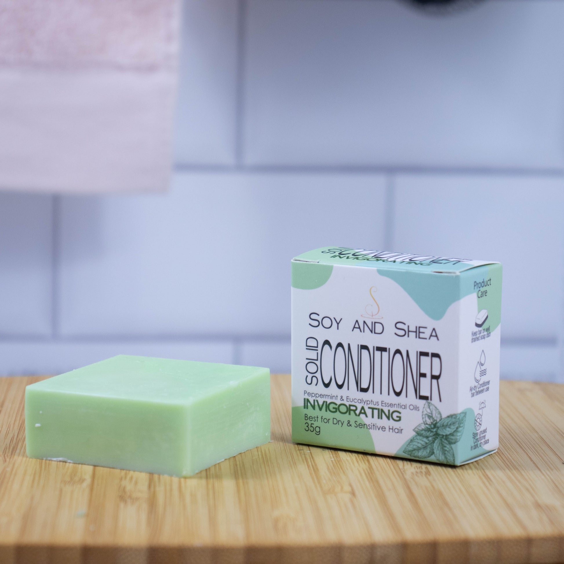 On a wooden tray sits a green bar of conditioner next to a white box with a green abstract pattern reading SOLID CONDITIONER against a blurred tiled background.