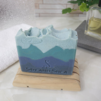 Blue and green layered soap on a wooden stand with 'Soy and Shea' branding.
