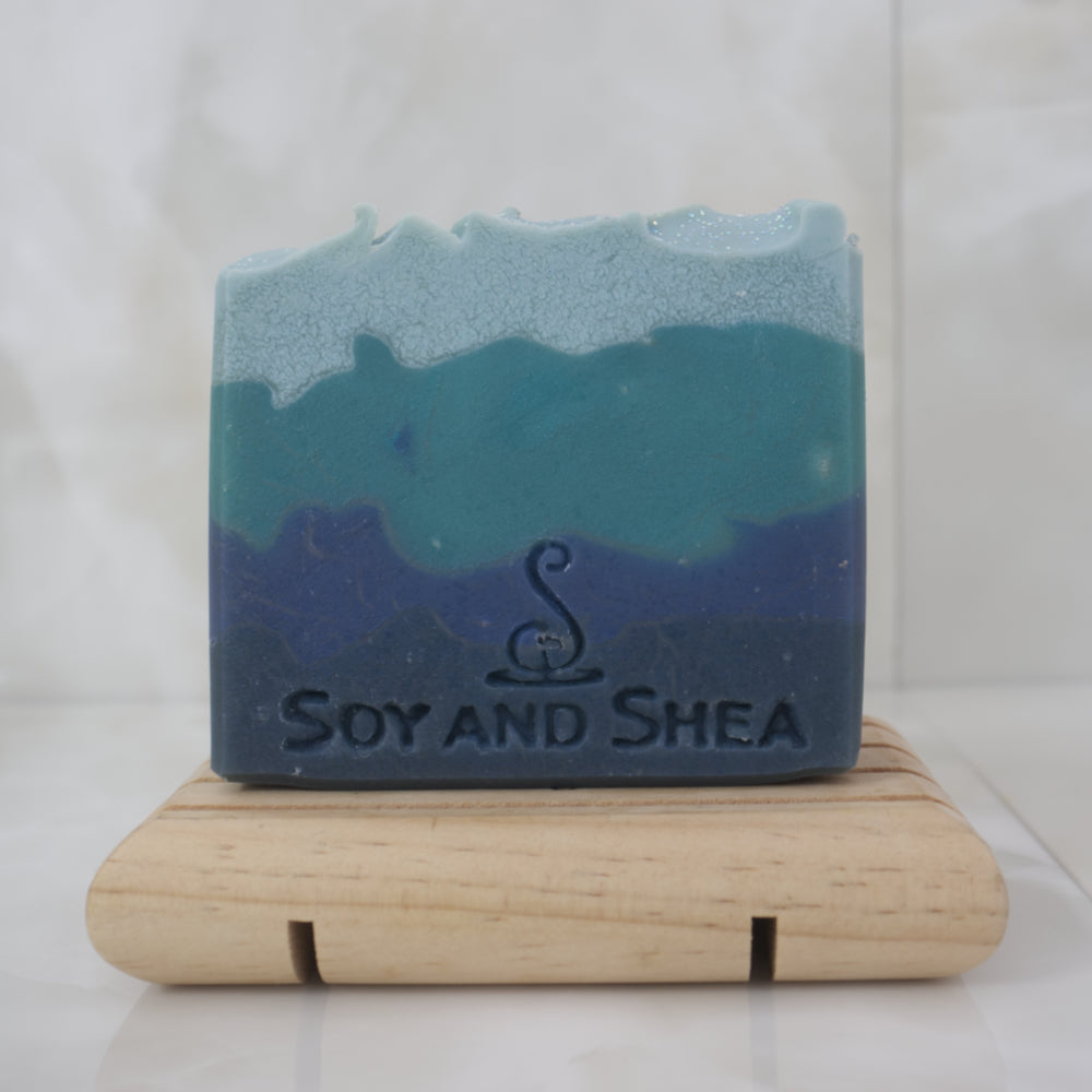Blue and green layered soap on a wooden stand with 'Soy and Shea' branding.