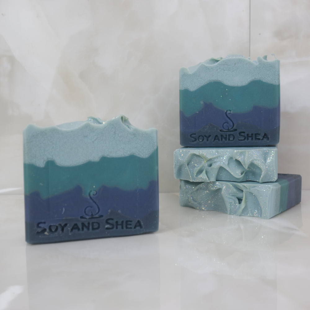 Blue and green layered soap bars with 'Soy and Shea' branding on a white background