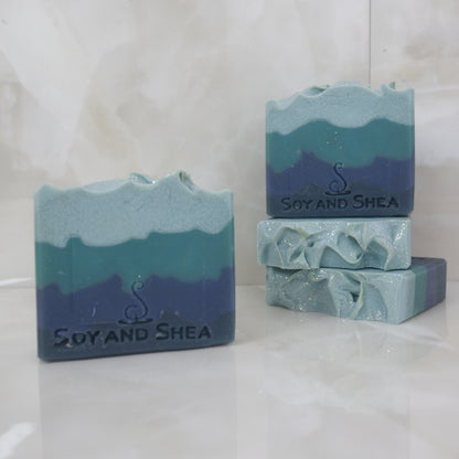 Blue and green layered soap bars with 'Soy and Shea' branding on a white background