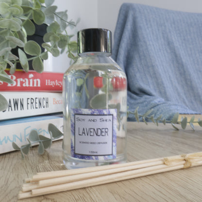 Soy and Shea Lavender Reed Fiffuser in glass bottle on a table with books and a plant in the background