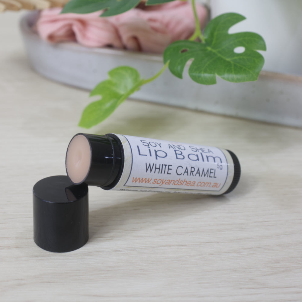 Black Lip balm tube with the lid off showing a tan balm inside.  The tube is wrapped with a white label with name of Lip Balm being White Caramel
