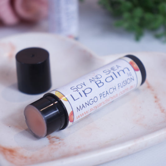 A black tube with white label reading LIP BALM lies on a stone dish with a blurred background.  The lid has been removed revealing a peach coloured balm and sits behind the tube.