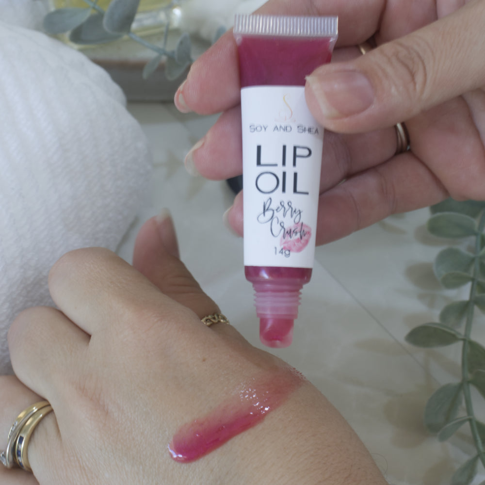 A hand holds a tube of Lip oil next to another hand that has a smear of the oil across the back demonstrating the colour and translucent nature of the oil.  The tube is clear showing a cerise Lip Oil that goes onto the hand with a sheer look.