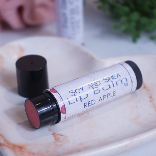 A black tube with white label reading LIP BALM lies on a stone dish with a blurred background.  The lid has been removed revealing a red balm and sits behind the tube.