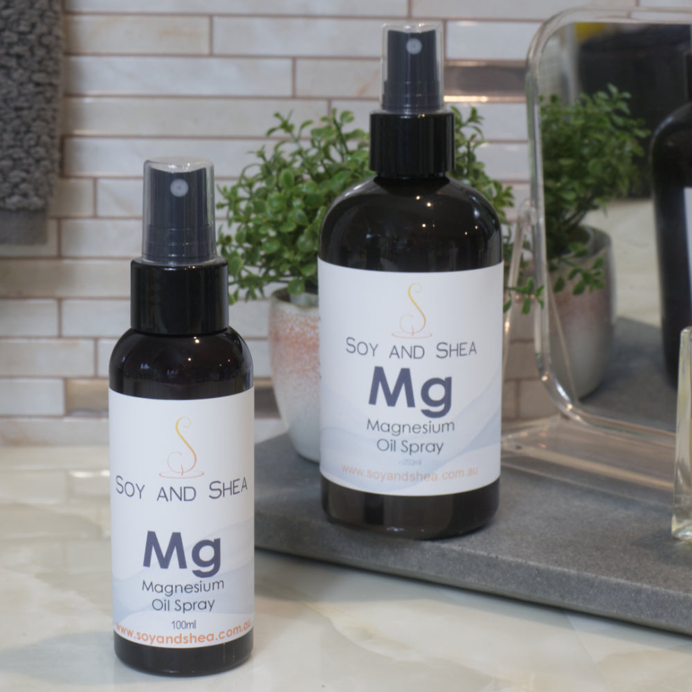 Two bottles of Soy and Shea Magnesium Oil Spray on a bathroom counter.  The bottles are amber in colour with a black spray nozzle and has a whote wrap around label.  The bottles are different sizes