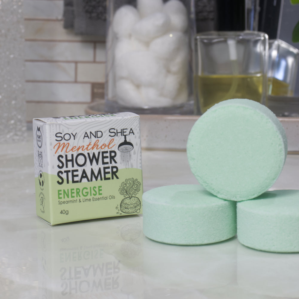 A box of Soy and Shea Menthol Shower Steamer labeled 'Energise' sits on a countertop next to three round, pale green shower steamer discs.