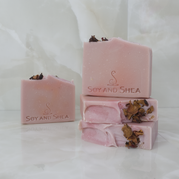 A collection of four Midnight Rose Soap bars sit on a marble background.  The soaps are a solid dusky pink colour with a small amount of dried rose petals on the top left corner