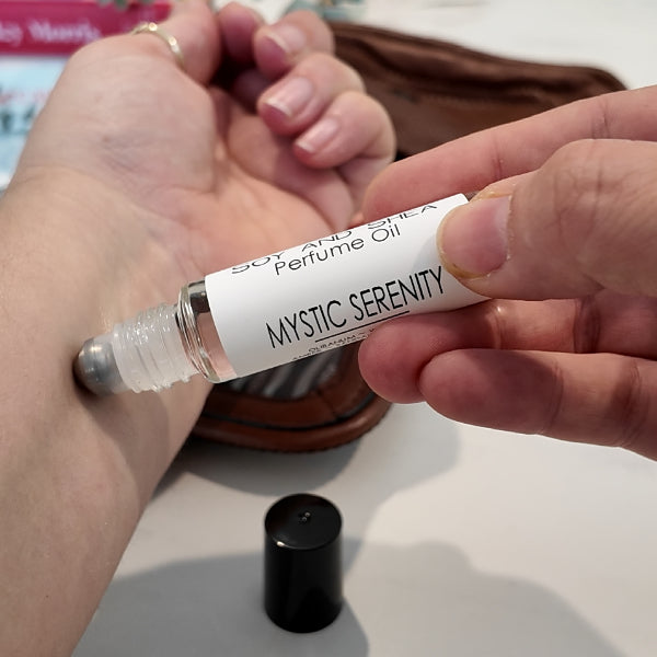 A person is applying a roller bottle of perfume oil labelled MYSTIC SERENITY to the other wrist. 