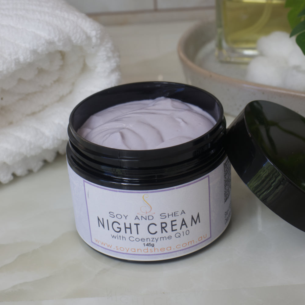 A black jar of Soy and Shea Night Cream with Coenzyme Q10 on a bathroom counter.    The cream is light purple