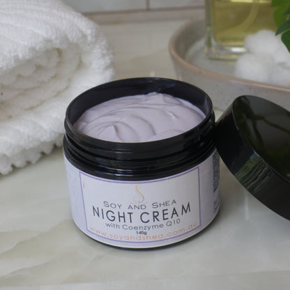 A black jar of Soy and Shea Night Cream with Coenzyme Q10 on a bathroom counter.    The cream is light purple