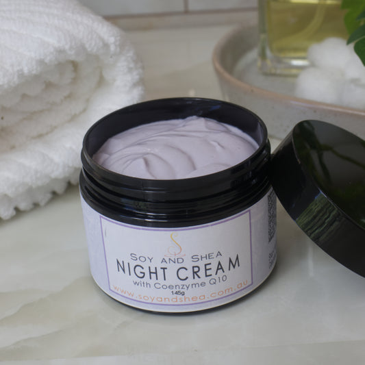 A black jar of Soy and Shea Night Cream with Coenzyme Q10 on a bathroom counter.    The cream is light purple