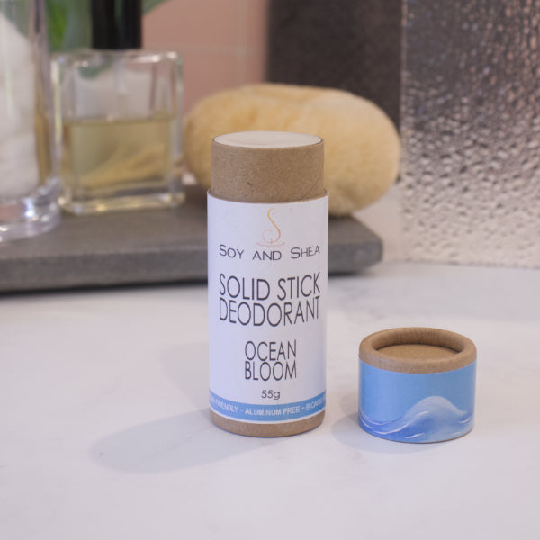 A cardboard tube labelled SOLID STICK DEODORANT stands upright on a bathroom counter top with a blurred background.  The lid of the tube sits to the left revealing the cream balm in the tube