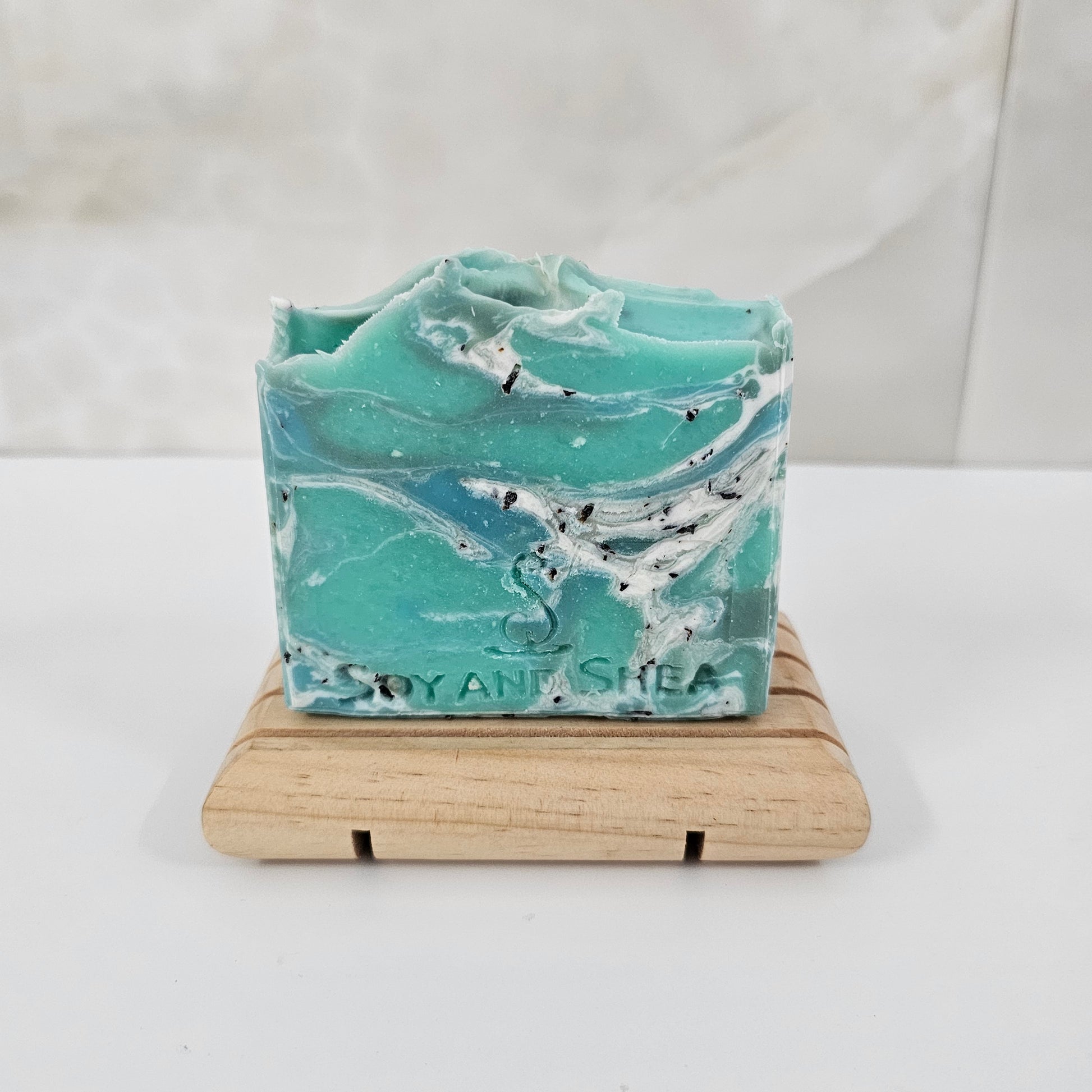 Green and white marble-patterned soap on a wooden soap dish against a white background