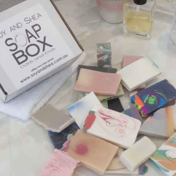 A selection of soap pieces lay scattered  across a bathroom counter next to a white box labelled SOAP BOX ODDS AND ENDS.  The soaps are various shapes and colours.